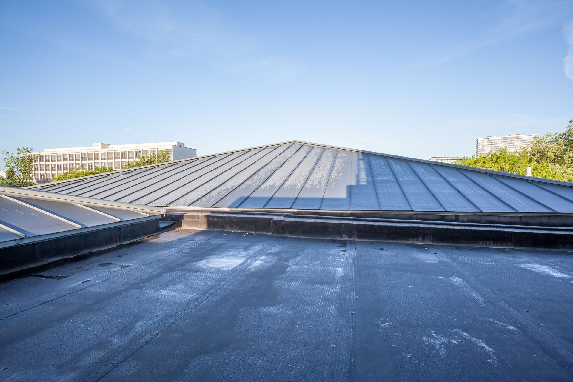 Flat rooftop with dark membrane and a sloped metal skylight under a clear blue sky