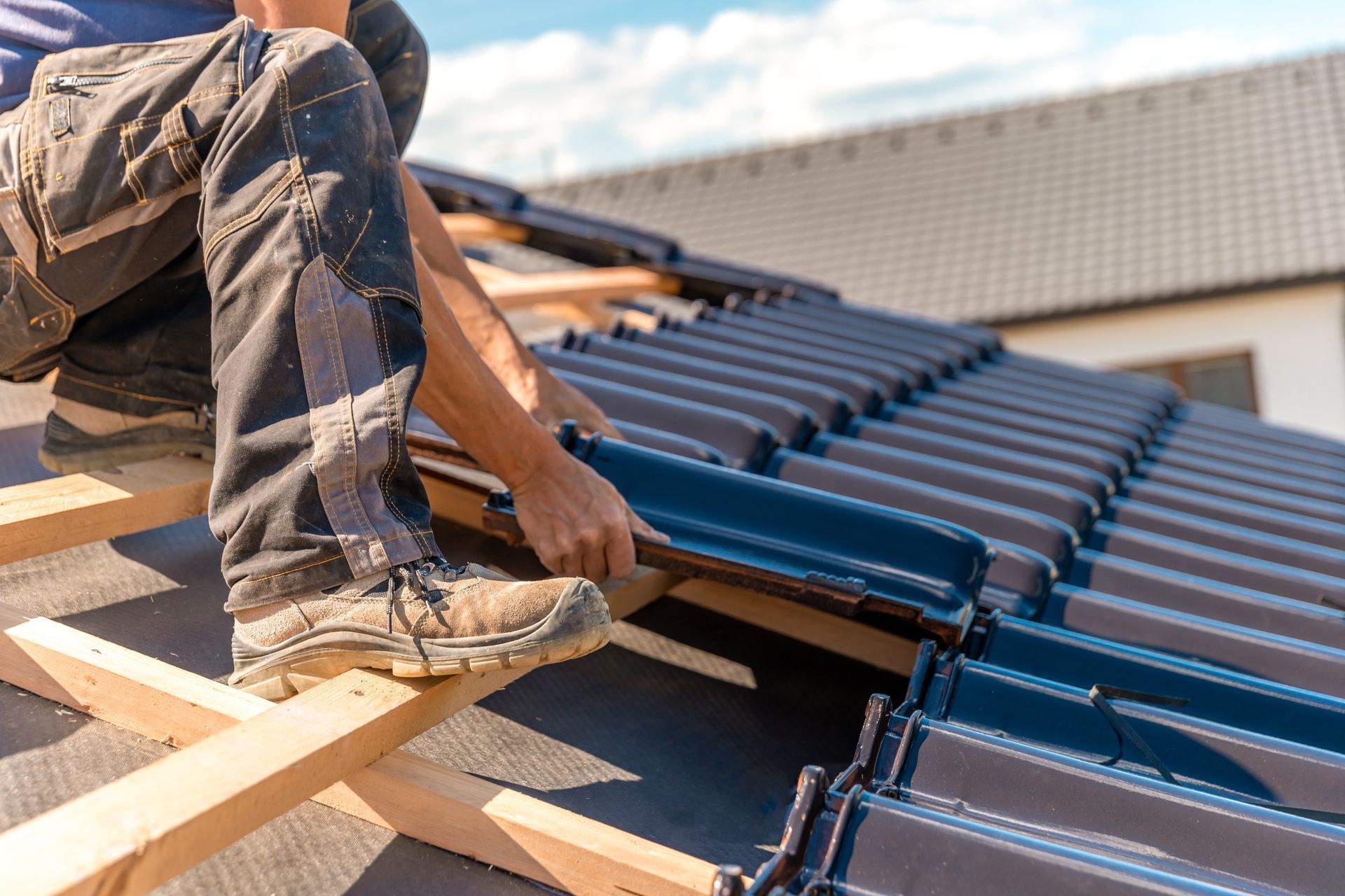 Worker installing blue roof tiles on a rooftop frame