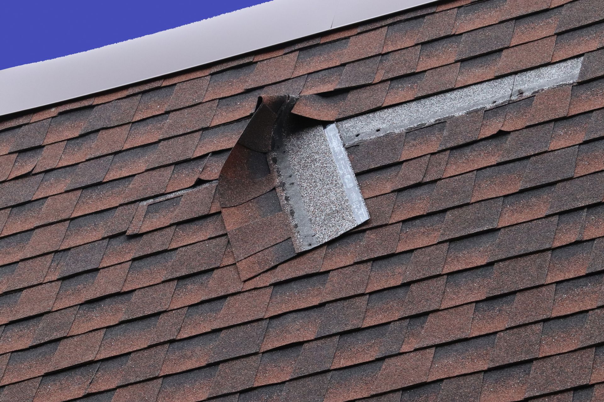 Damaged shingle roof with a bent metal vent pipe sticking out near the ridge