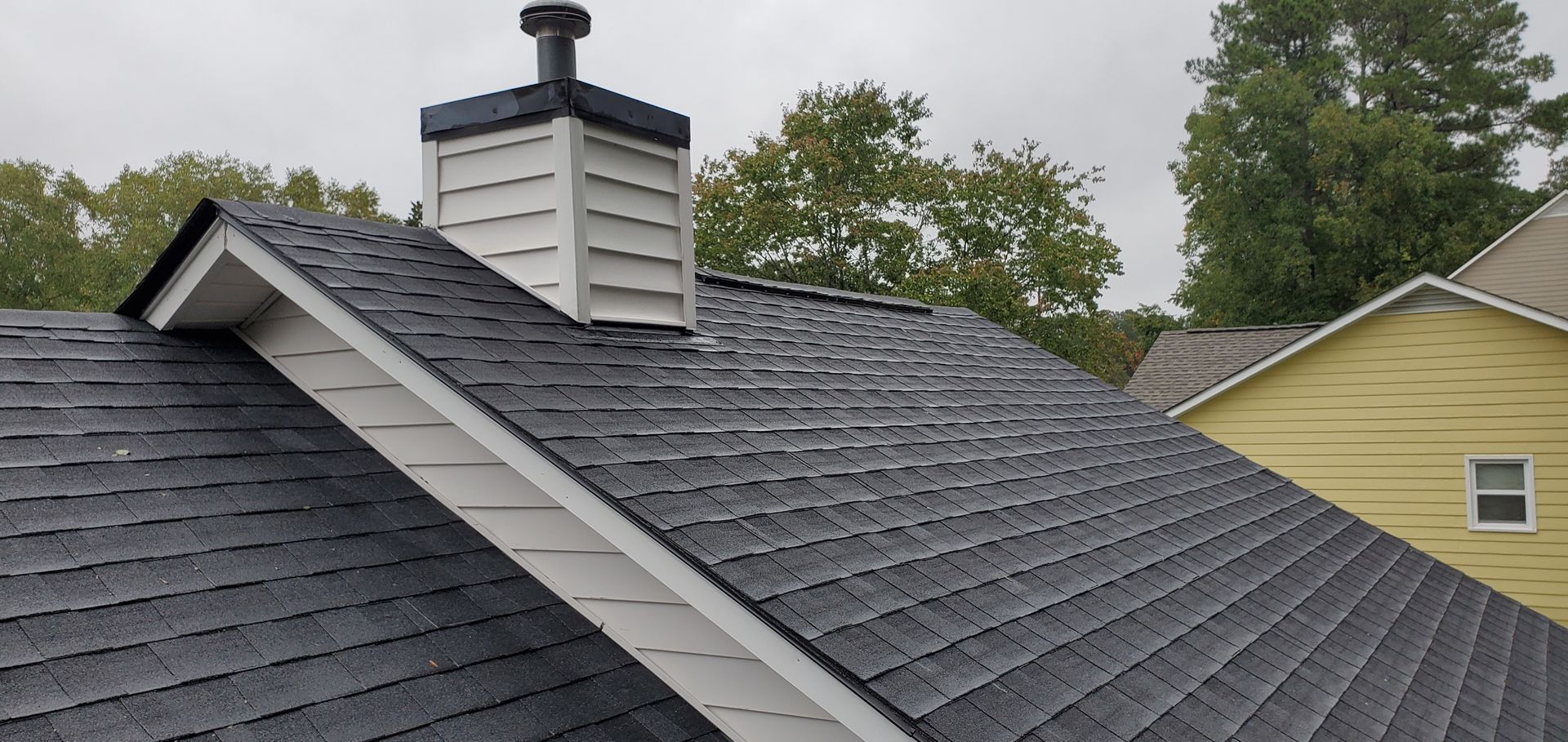 Shingled roof with a chimney and vent stack on a house under overcast skies