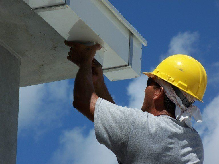 Construction worker in yellow hard hat inspecting or repairing an overhang against a blue sky