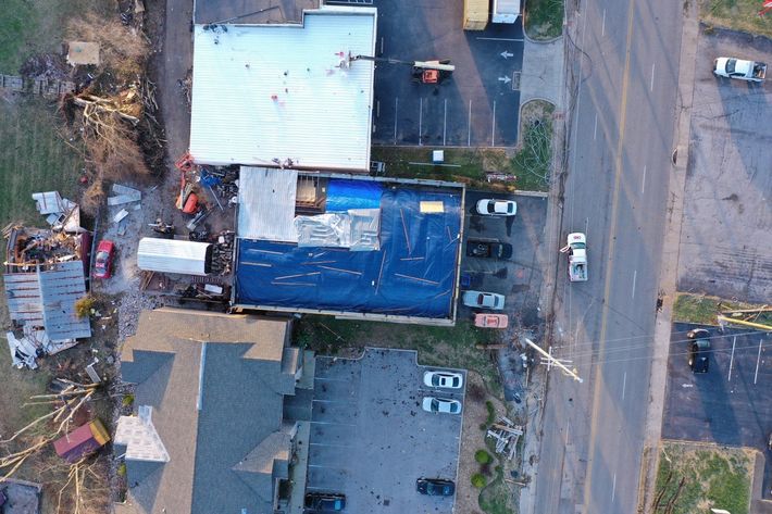 Aerial view of a building and parked cars beside a road, with tarps covering part of the roof.