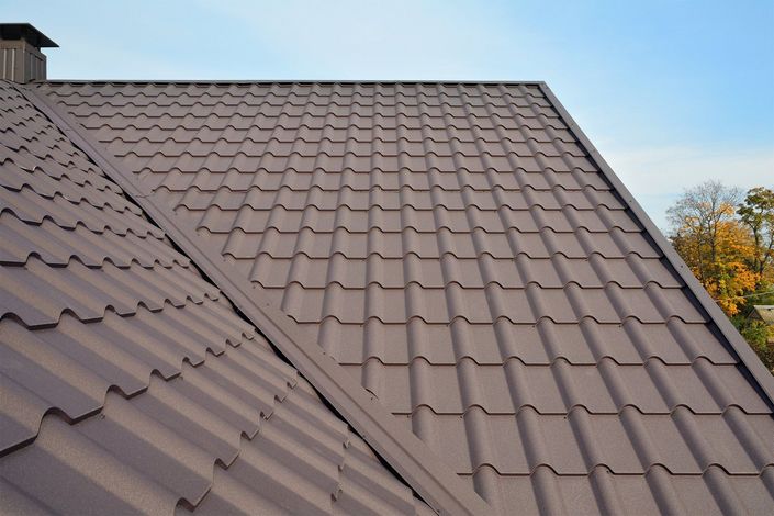 Brown metal roof with intersecting sloped sections against a blue sky