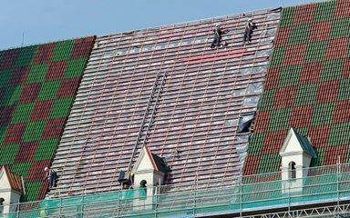 Colorful tiled roof with several dormer windows and chimneys, viewed from above