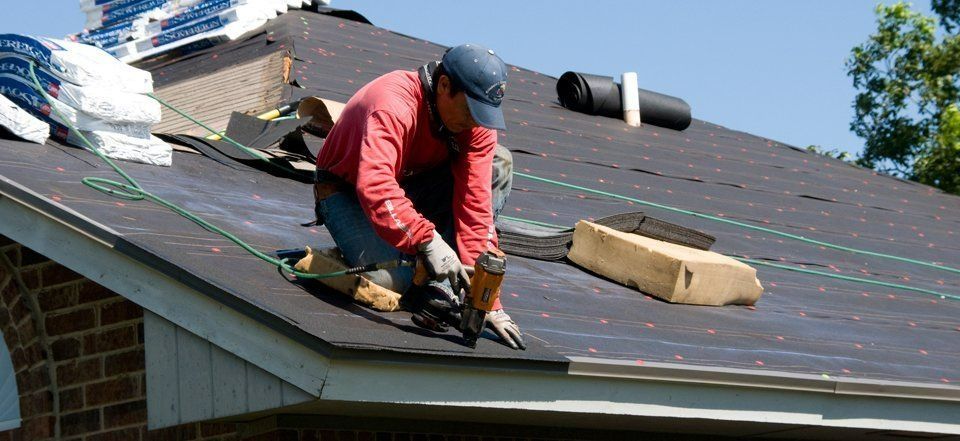 Worker in red jacket installing roofing on a sloped house roof with tools and materials nearby
