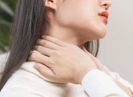 A zoomed in picture of a lady with dark shoulder length hair and her hands around her neck like she is massaging herself. 