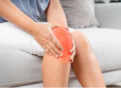 A zoomed in image of a person sitting on a white couch with their hands wrapped around their right knee.