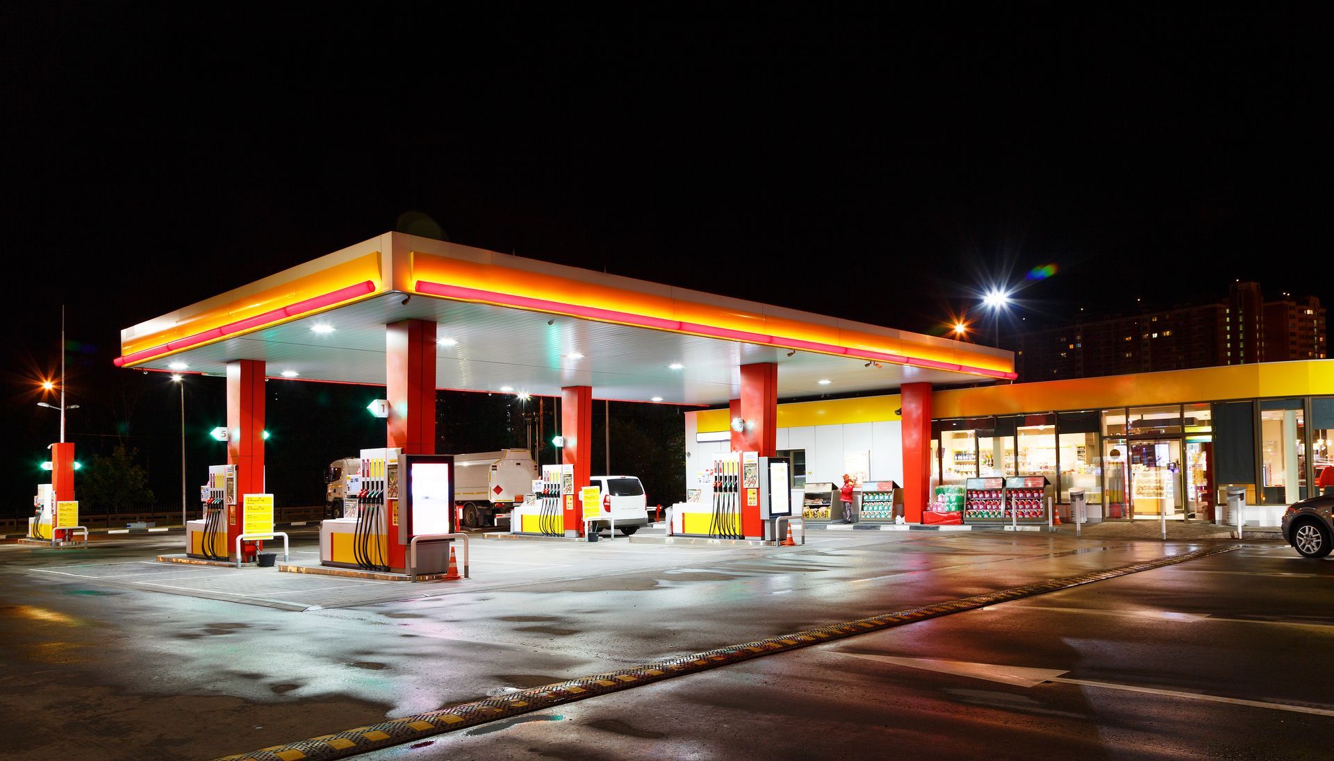 Nighttime view of a lit gas station with several fuel pumps and a convenience store canopy
