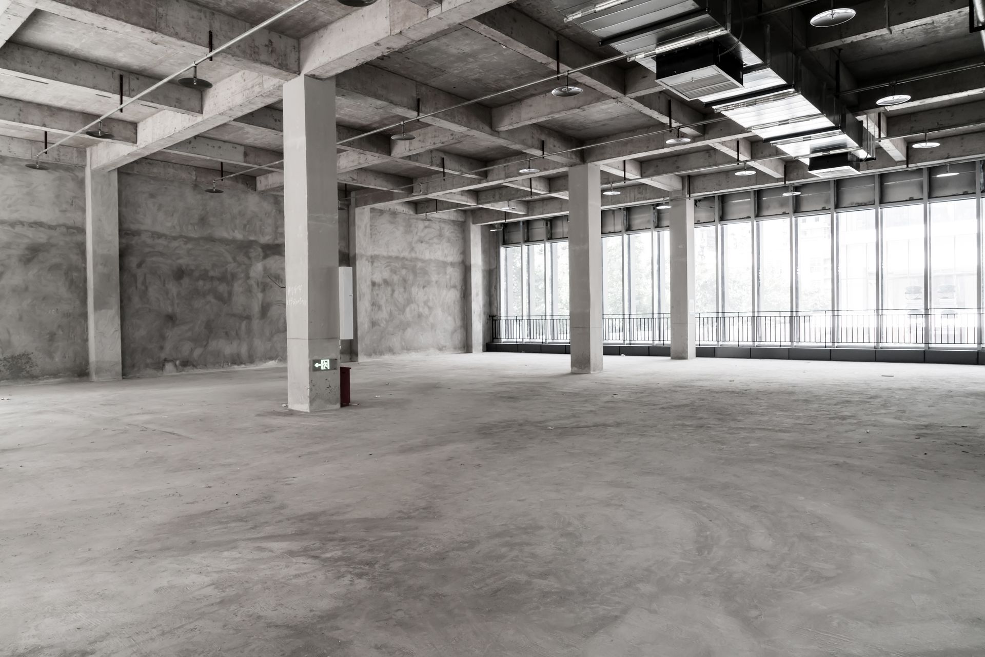 Empty unfinished concrete warehouse interior with exposed beams and large windows