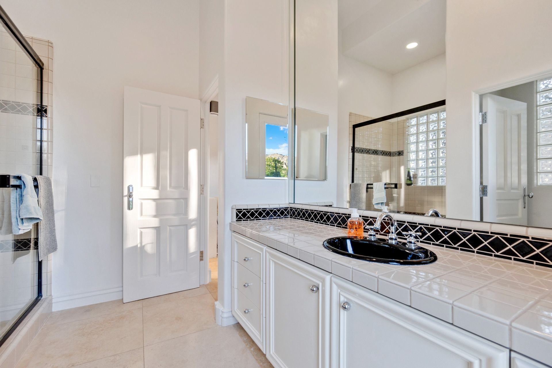 Bright bathroom with white cabinets, black countertop, double sinks, and a glass shower enclosure