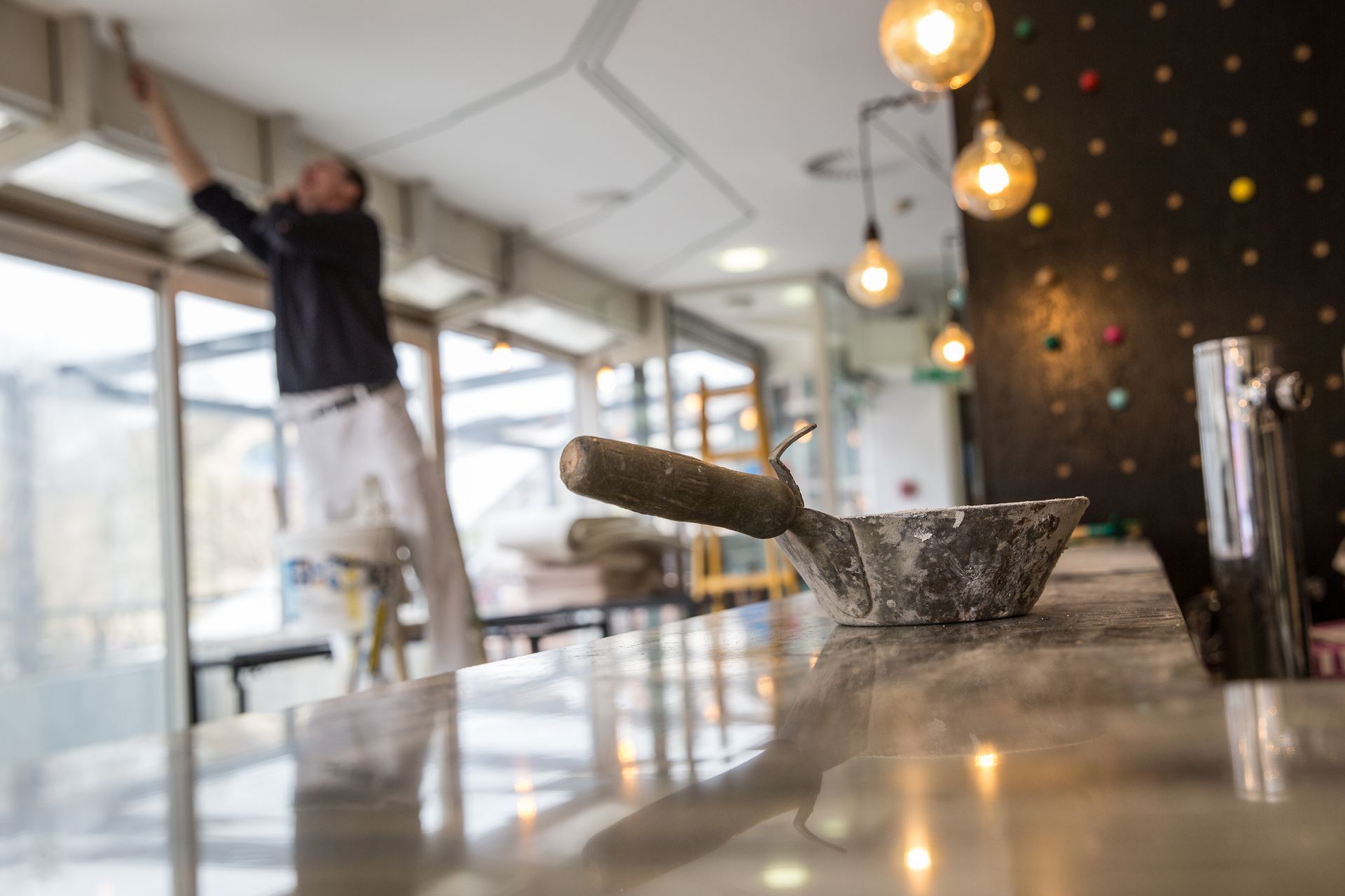 Worker painting an interior wall with a roller in a bright, modern room