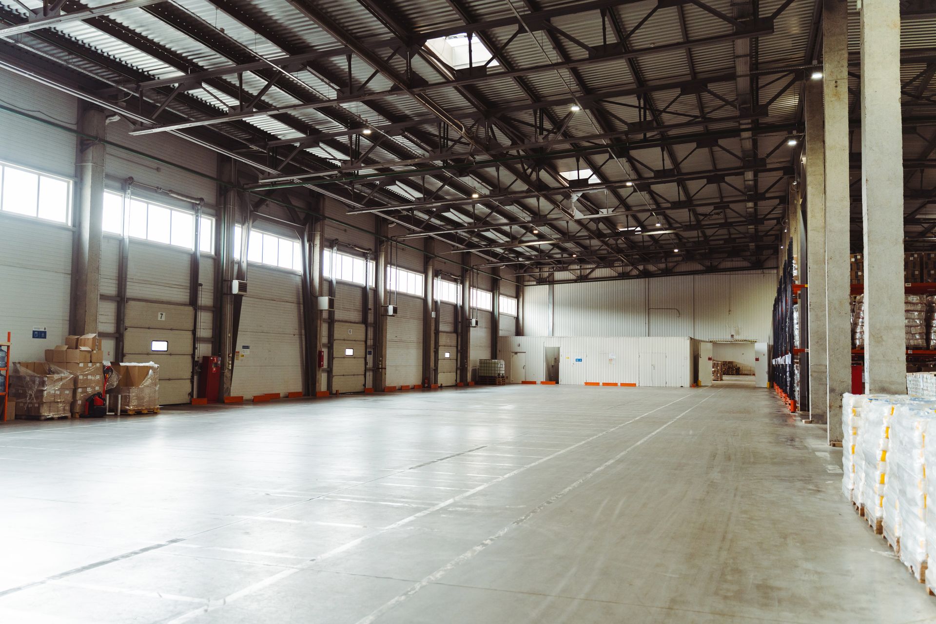 Empty warehouse interior with a large open concrete floor and stacked boxes along the walls