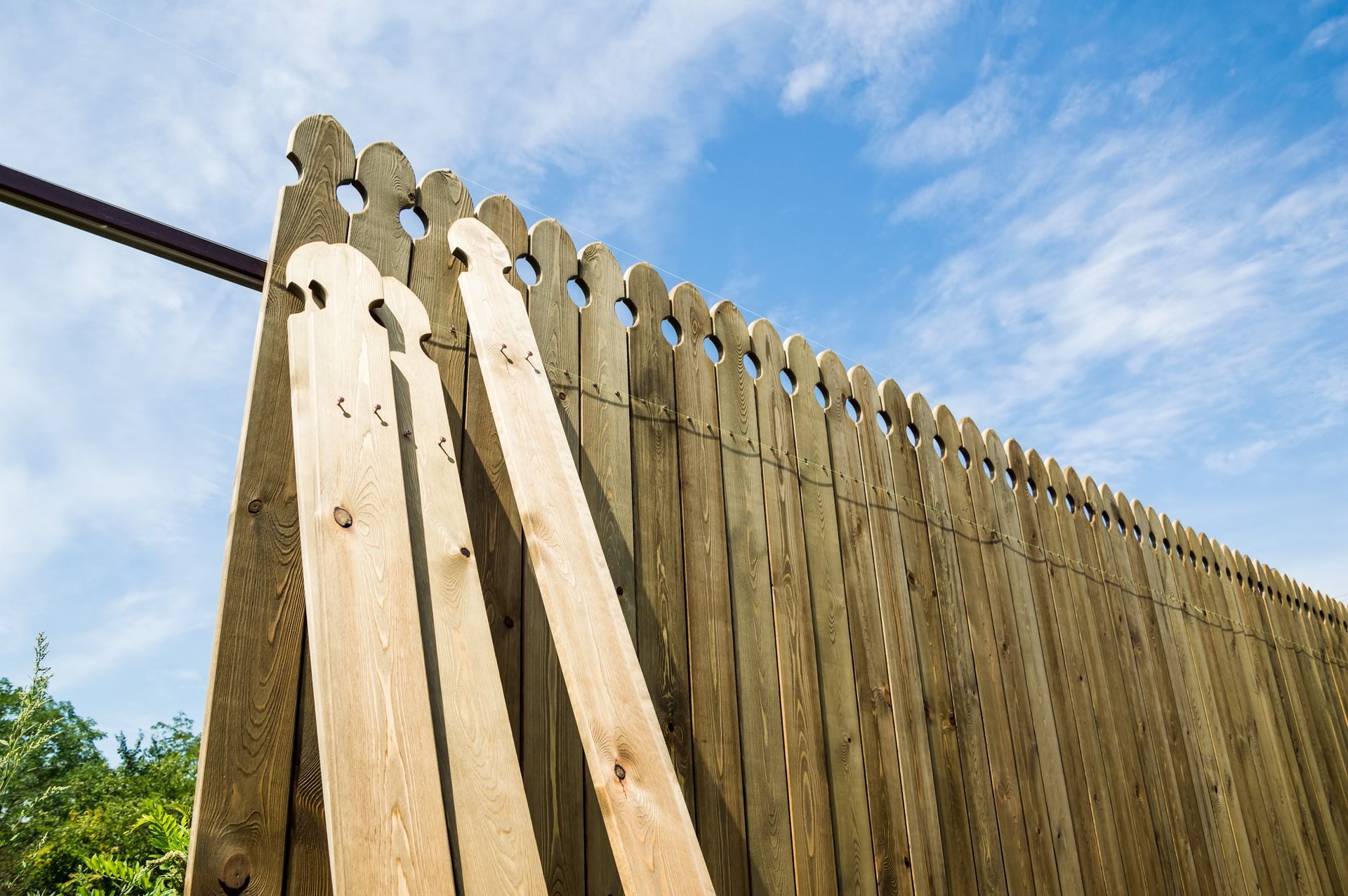 Wooden fence with pointed tops and two leaning boards against a blue sky
