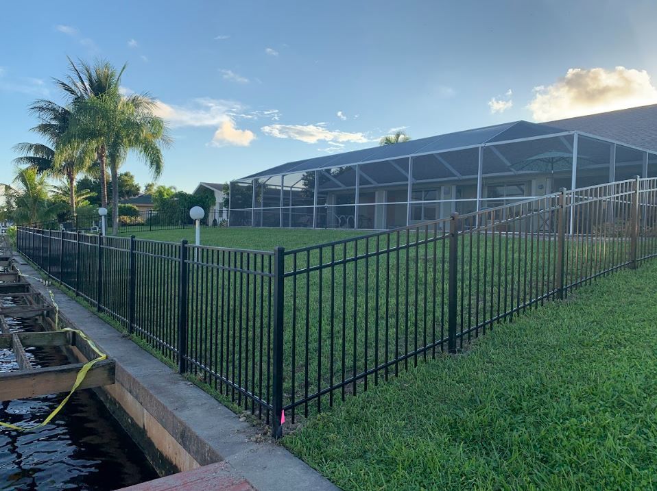 Black metal fence around a grassy backyard, adjacent to a canal, under a blue sky.