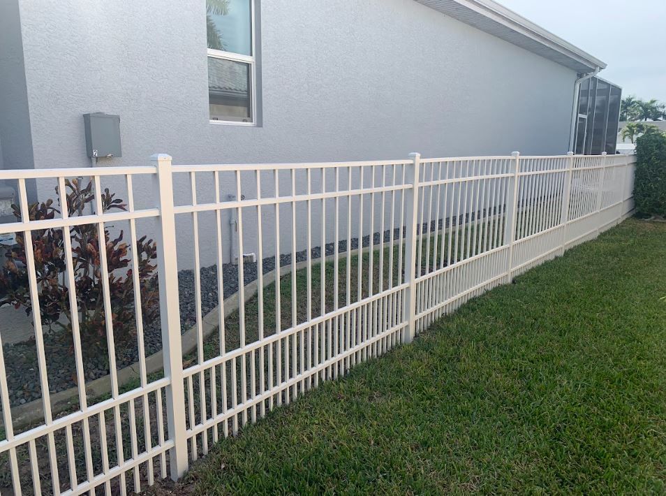 White metal fence bordering a house with gray stucco, on a green lawn.