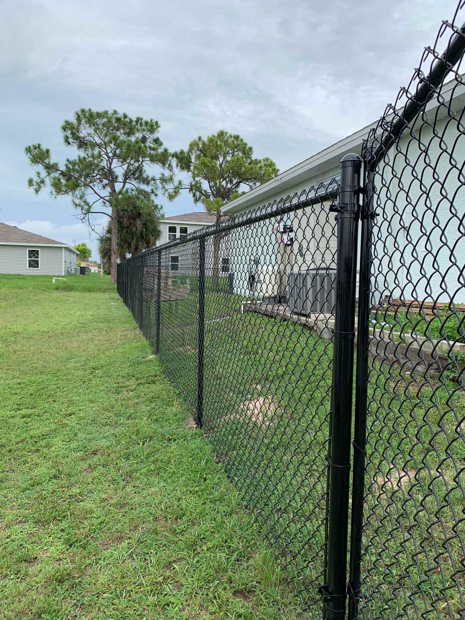 Black chain-link fence in backyard with green grass, under cloudy sky.