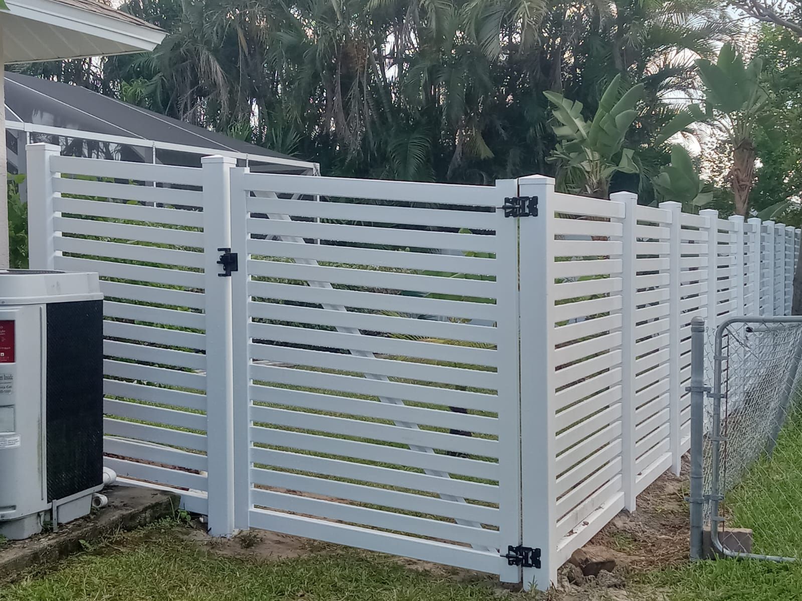 White horizontal slatted fence and gate enclosing a yard, with black hardware.