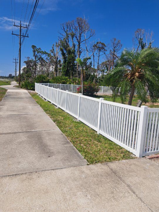 White picket fence along a paved road, under a clear blue sky.