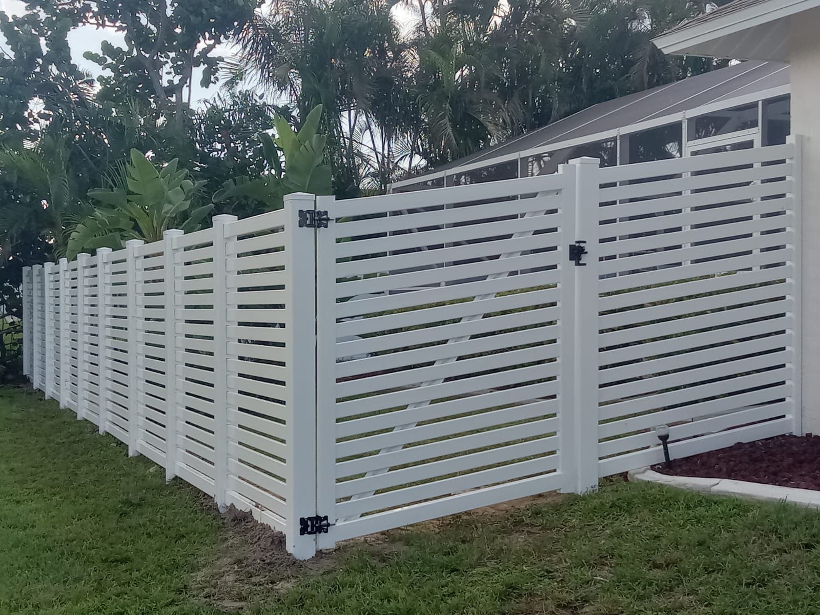 White horizontal slat fence with gate in grassy yard.