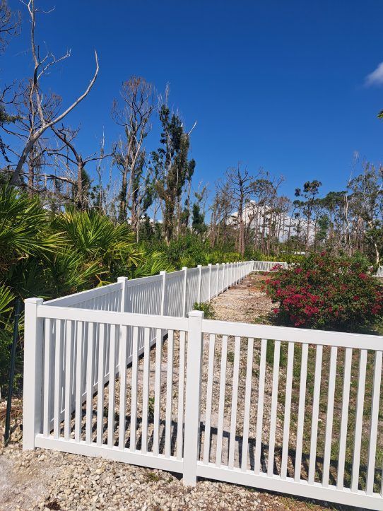 White picket fence with gate, gravel path, and blue sky.