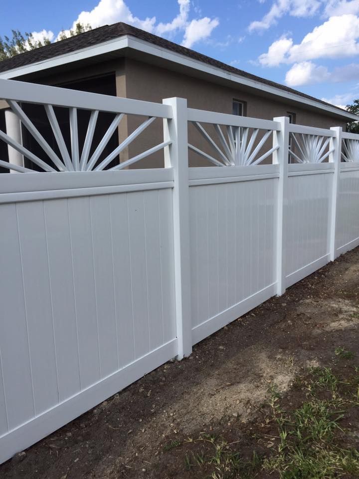 White vinyl fence with sunburst design at top, beside a brown building.