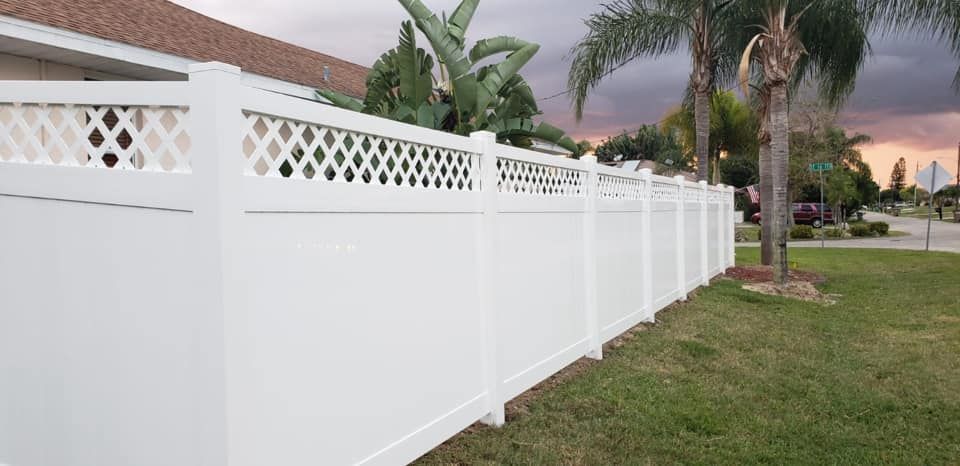 White vinyl fence with lattice top, along green grass and a residential street, under cloudy sky.