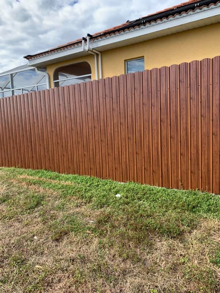 Brown vertical-slat fence alongside a yellow house with a green grassy lawn.