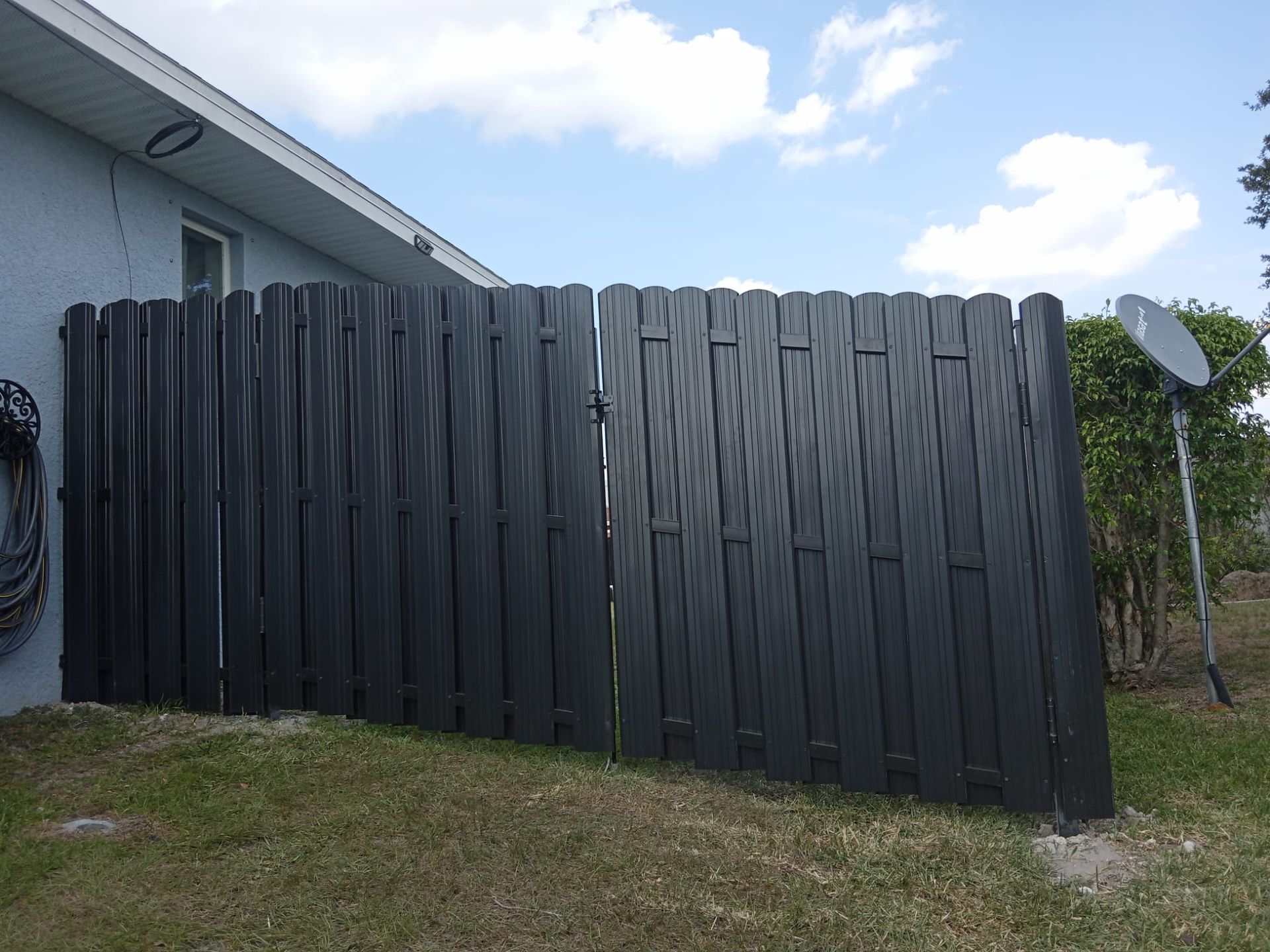 Black wooden fence attached to a building, with a gate, on a grassy lawn under a blue sky.