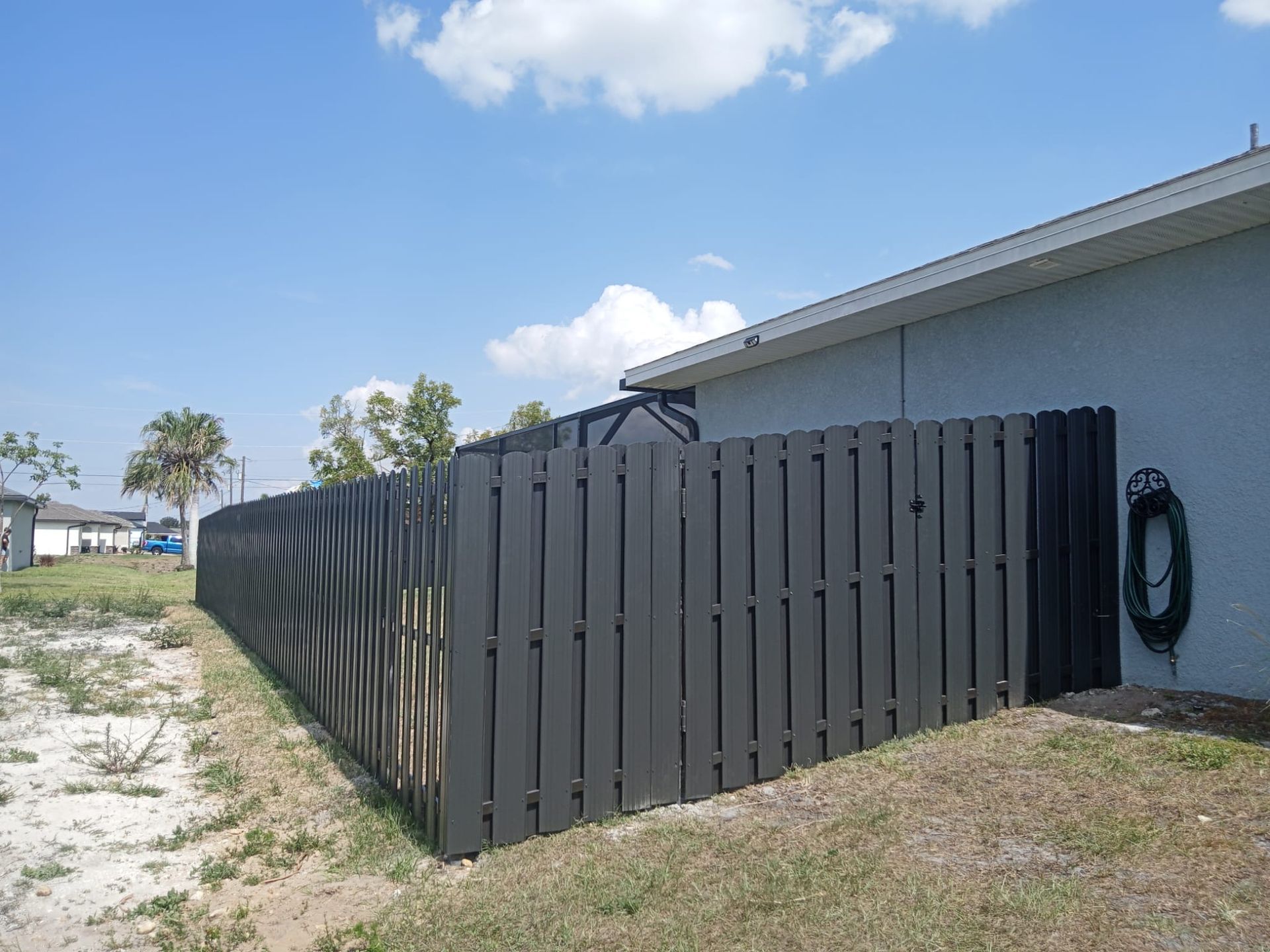 Black wooden fence beside a light-colored house under a partly cloudy blue sky.