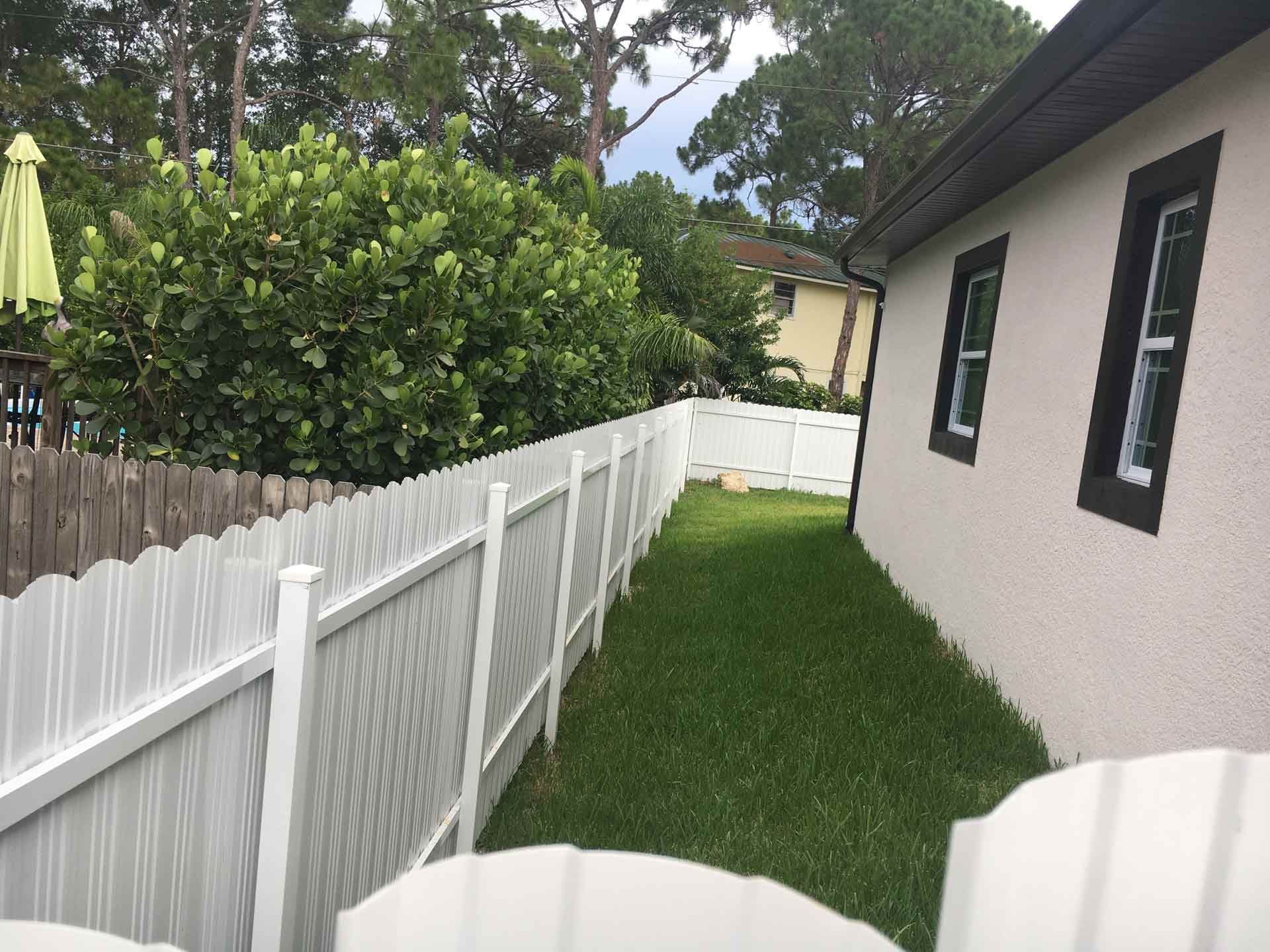 White scalloped fence along a grassy yard next to a beige house with dark window trim.