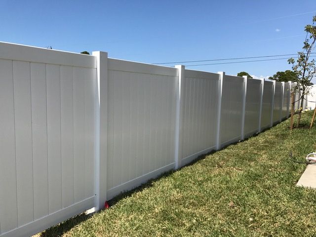 White vinyl fence along green grass under a blue sky.