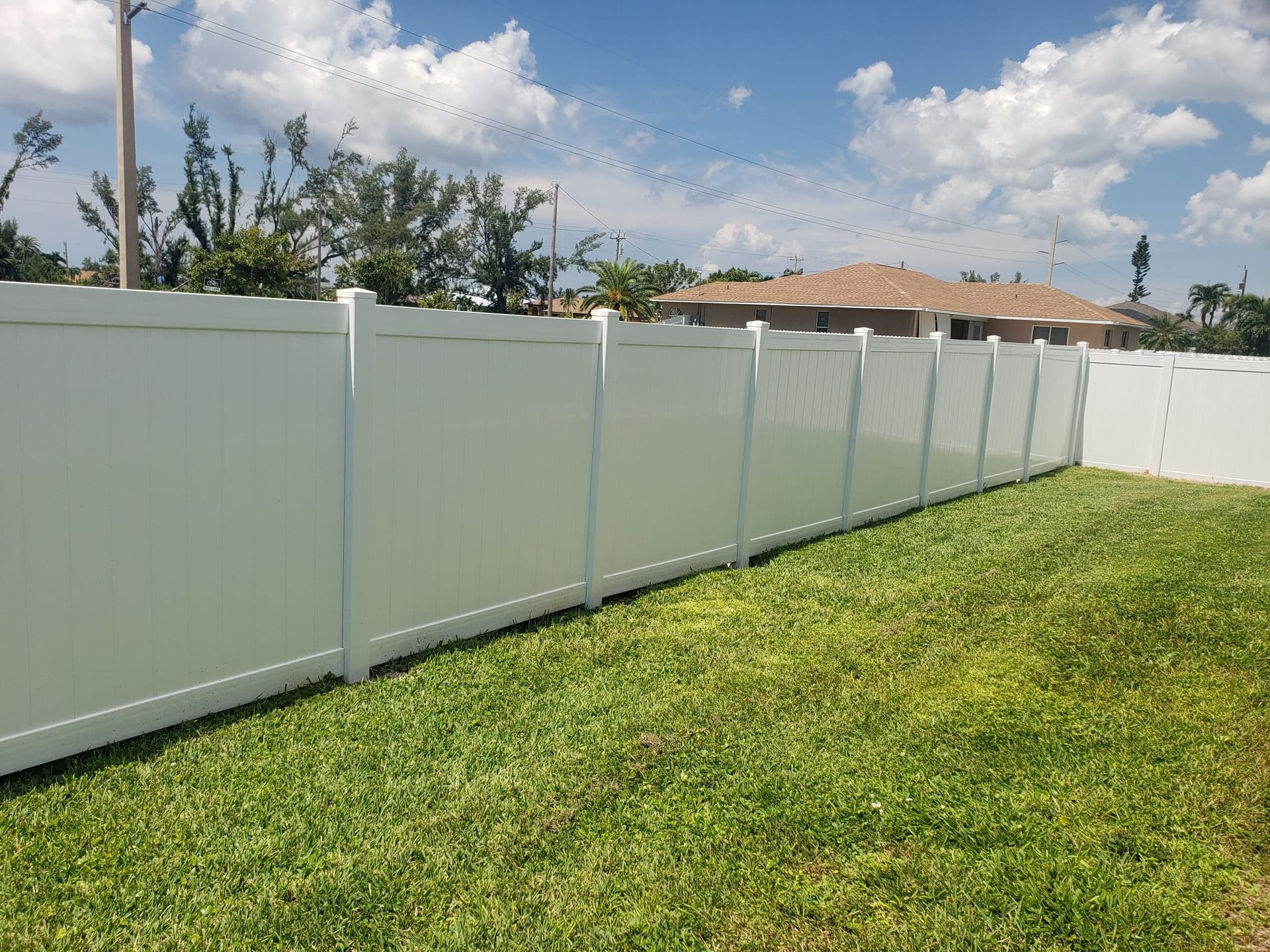White vinyl fence along green grass yard with blue sky and clouds.