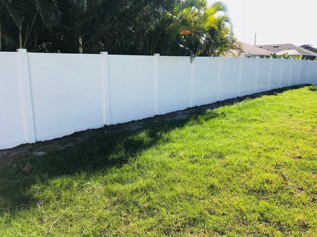 White vinyl fence along green grass. Trees and a house are in the background.