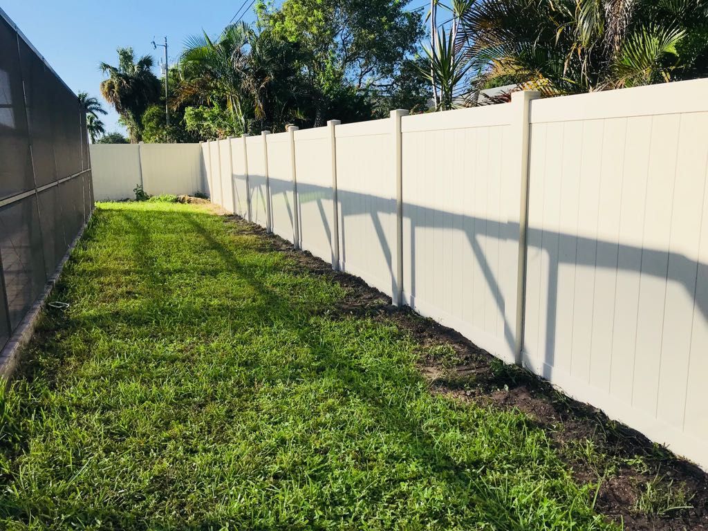 Lawn with white fence on the right and chain link fence on the left. Green grass with long shadows. Sunny day.
