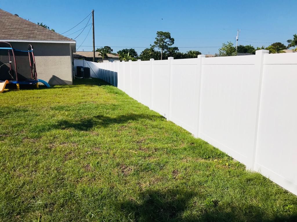 White vinyl fence bordering a grassy backyard on a sunny day.