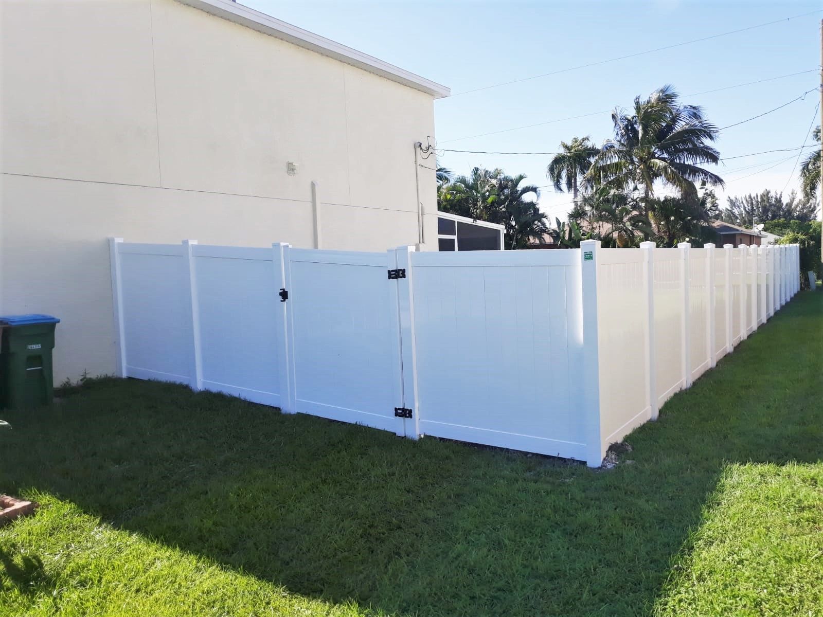 White vinyl fence along green grass, with gate and a building in the background.