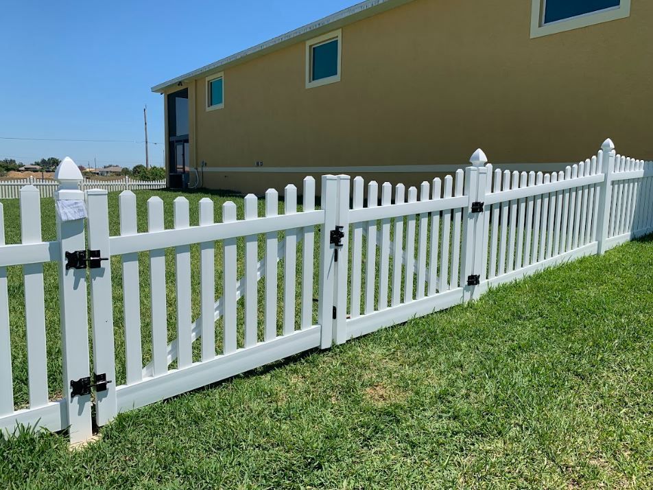 White picket fence in front of a beige house on a sunny day.