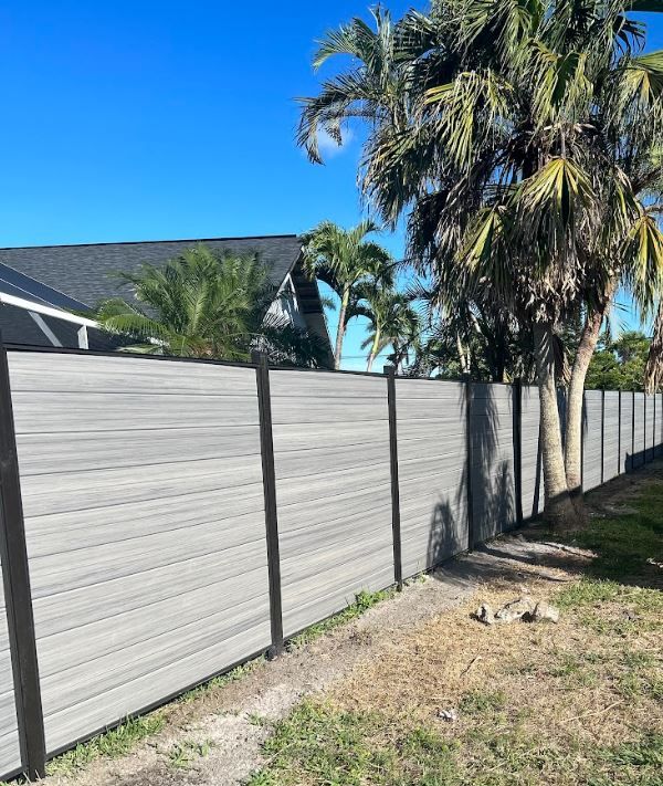 Gray horizontal slat fence with black posts, palm trees, and clear blue sky.