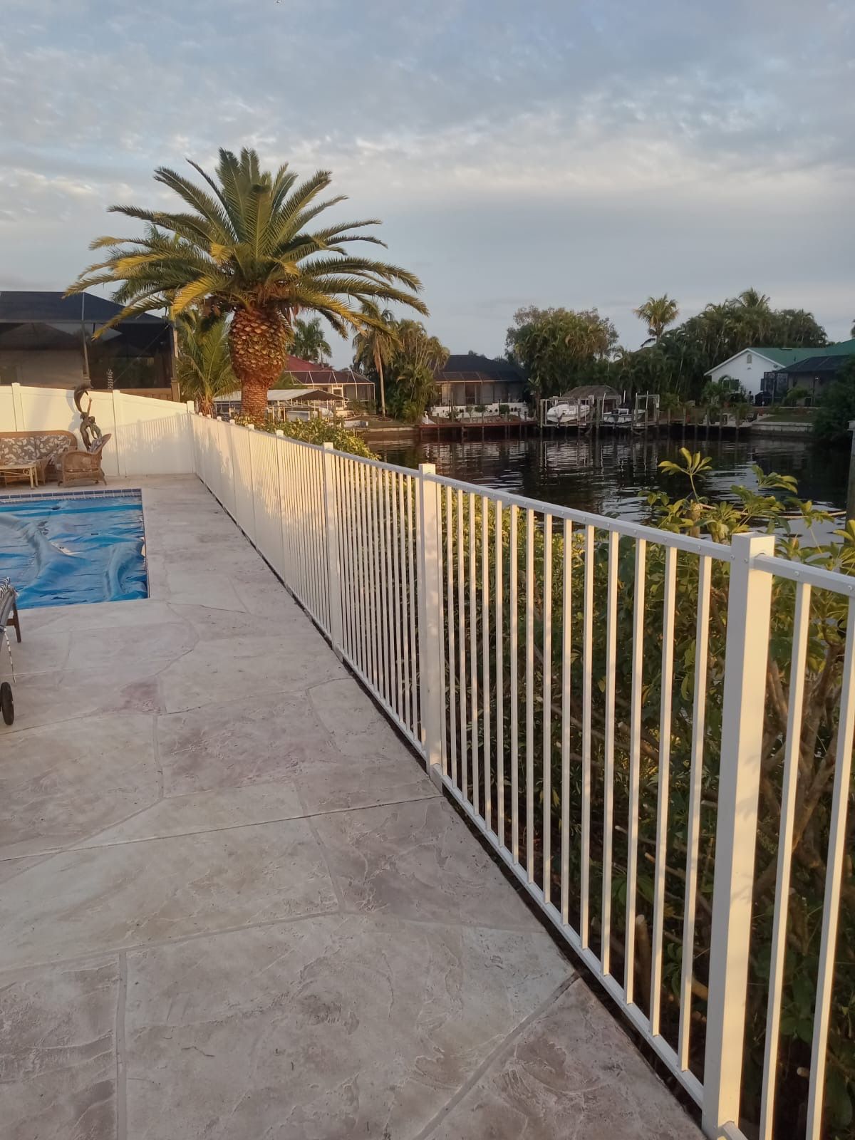 White fence along a canal, palm tree, and part of a pool on a sunny day.