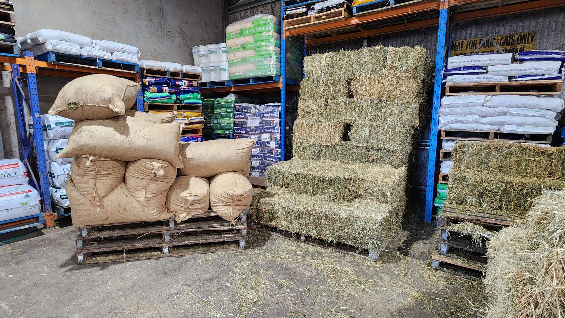 A Pile Of Hay Is Sitting On Top Of A Pallet In A Warehouse With Chaff Bags Next To It — Cooroy Produce In Cooroy, QLD