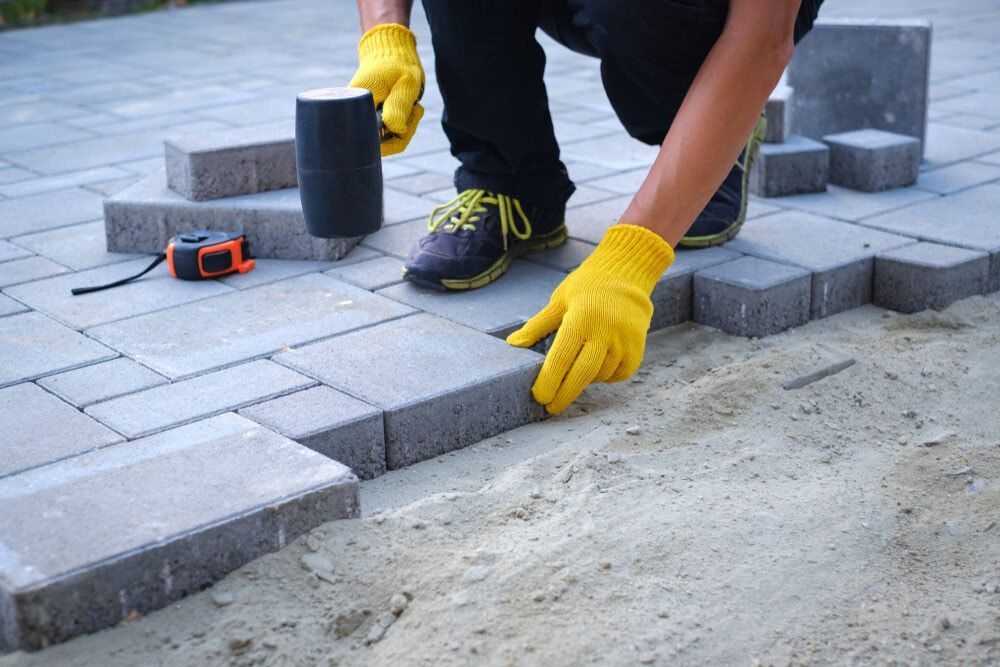 A Man Wearing Yellow Gloves Is Laying Bricks On A Sidewalk — Cooroy Produce In Cooroy, QLD