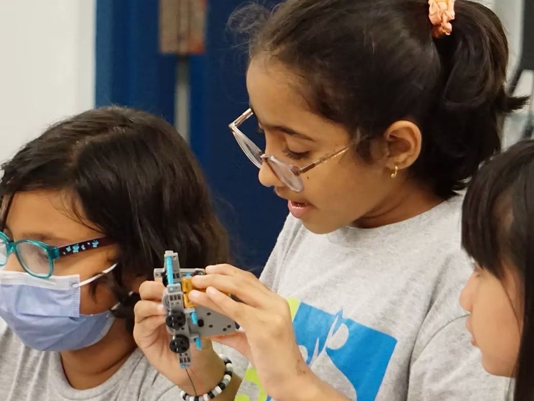 A group of young girls wearing masks and glasses are working on a robot. A group of young girls wearing masks and glasses are working on a robot.