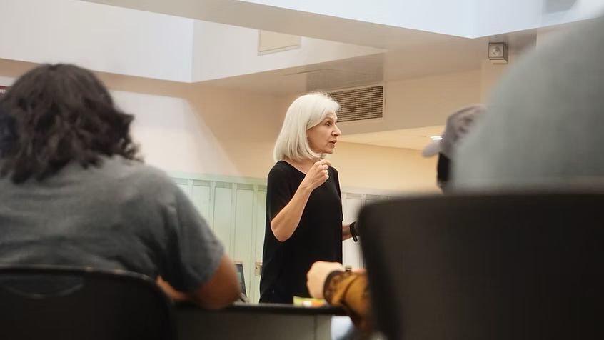 A woman is giving a lecture to a group of people in a classroom.