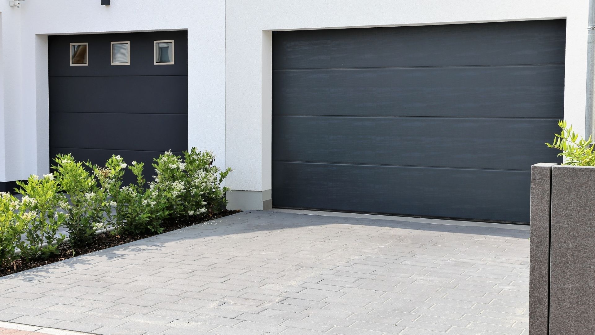 A white house with two black garage doors and a driveway.