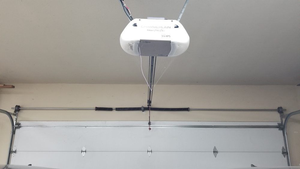 A garage door opener is hanging from the ceiling above a garage door.