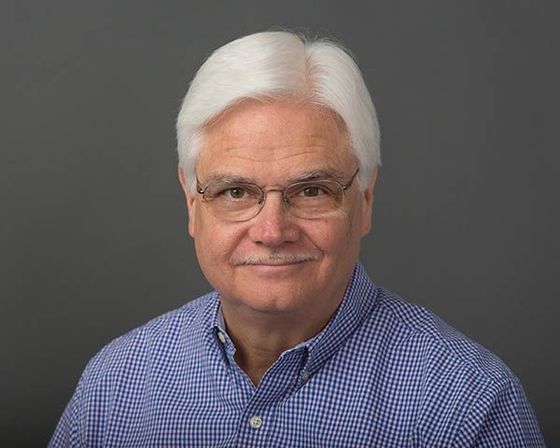 A man with white hair and glasses is wearing a blue plaid shirt.