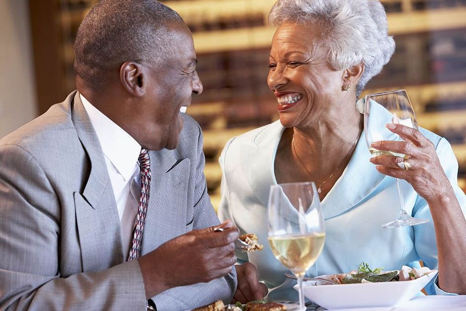 A man and woman are sitting at a table eating and drinking wine.