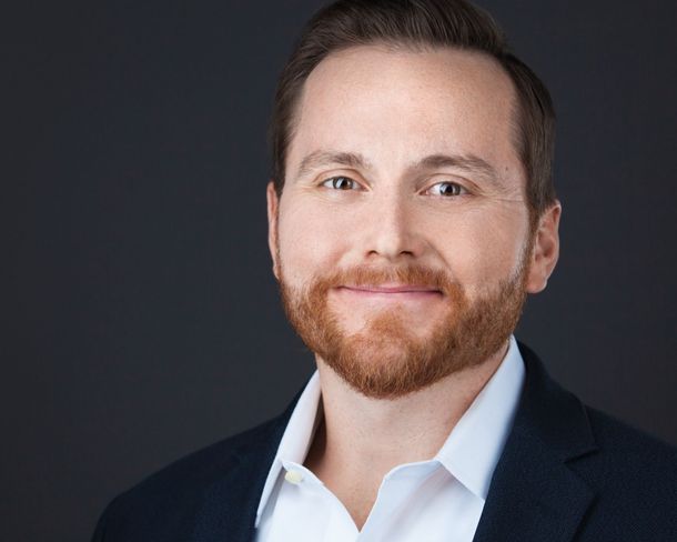 A man with a beard is wearing a suit and white shirt.