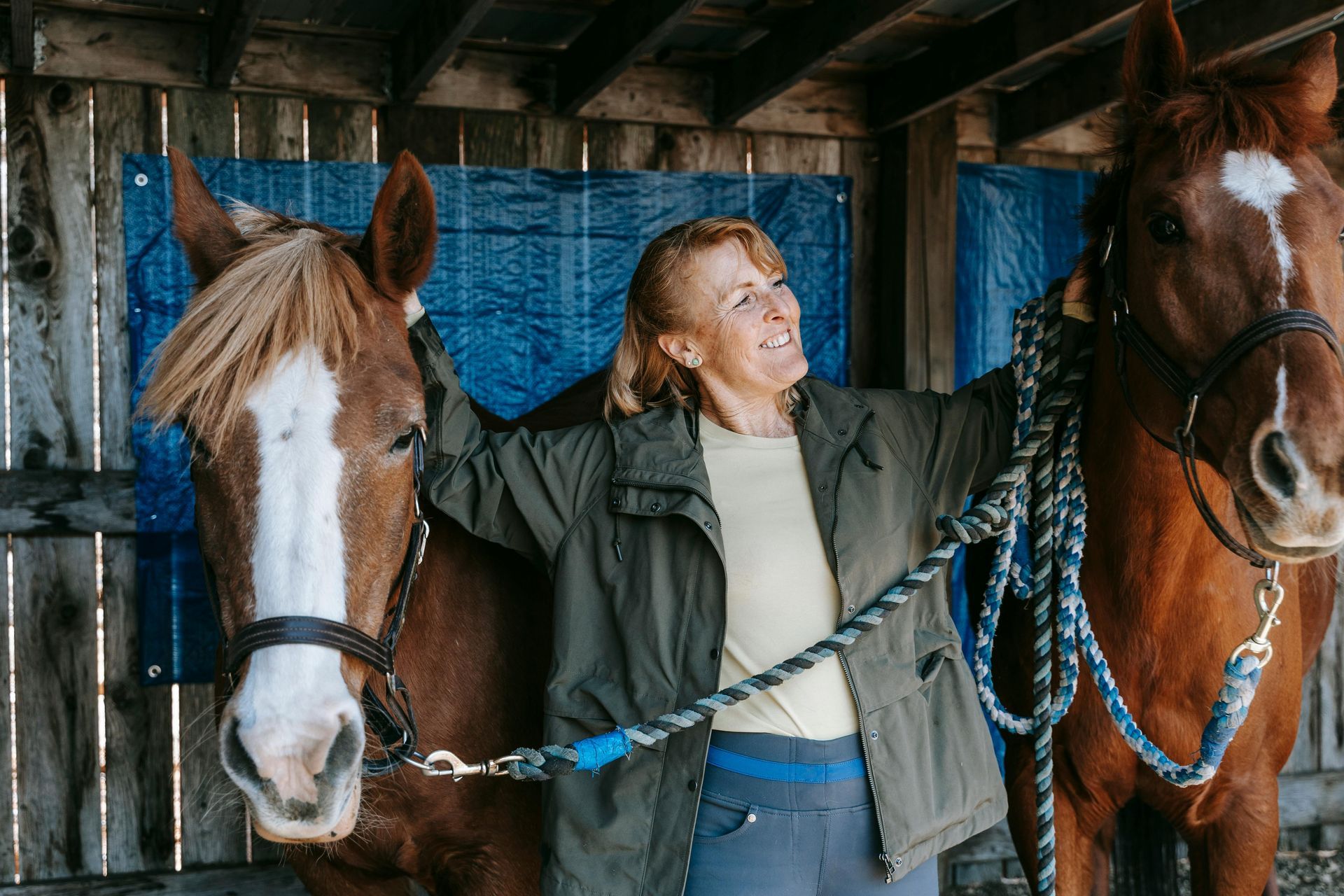 A woman is standing next to two horses in a stable.