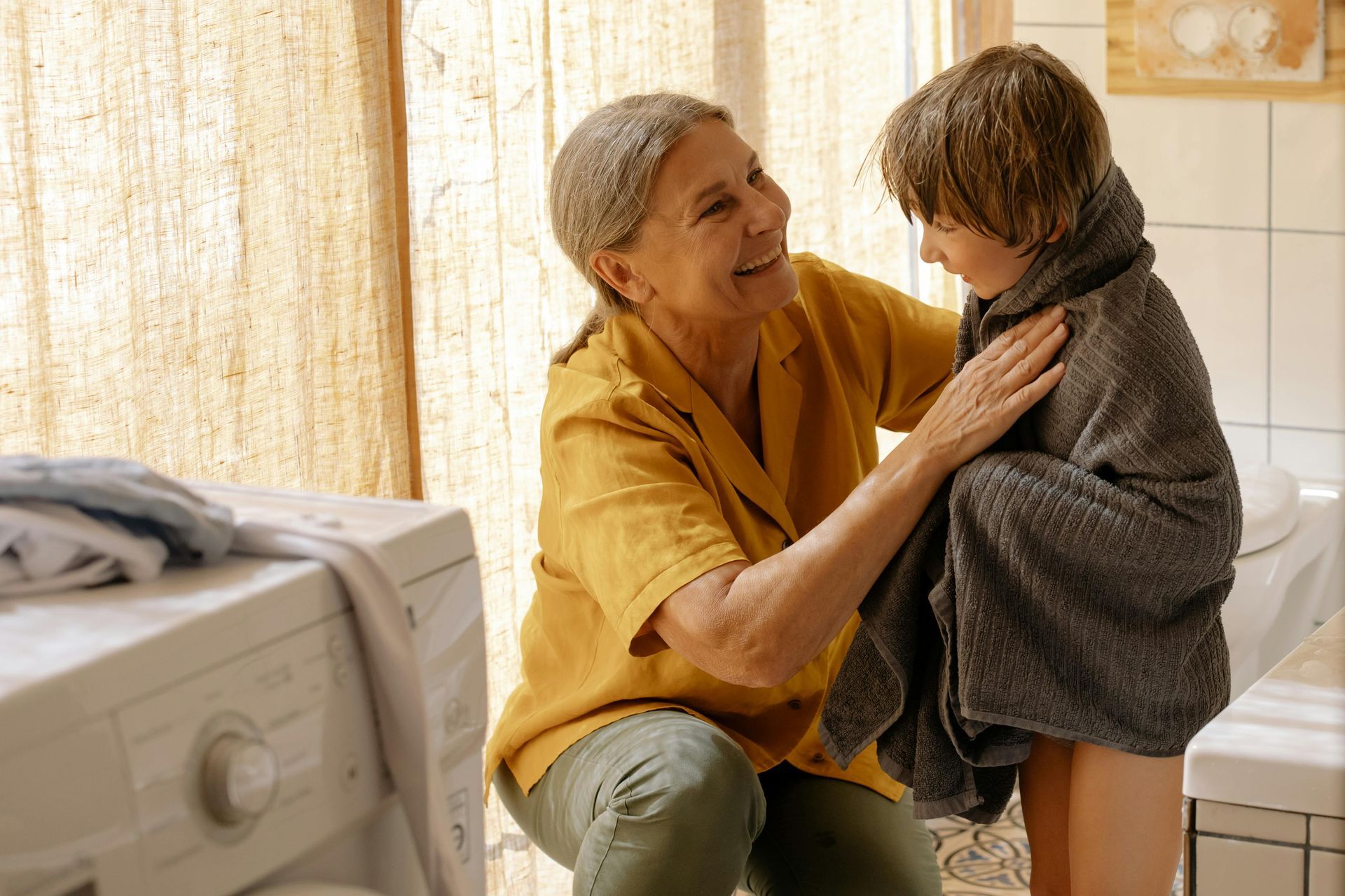 A woman is wrapping a child in a towel in a bathroom.